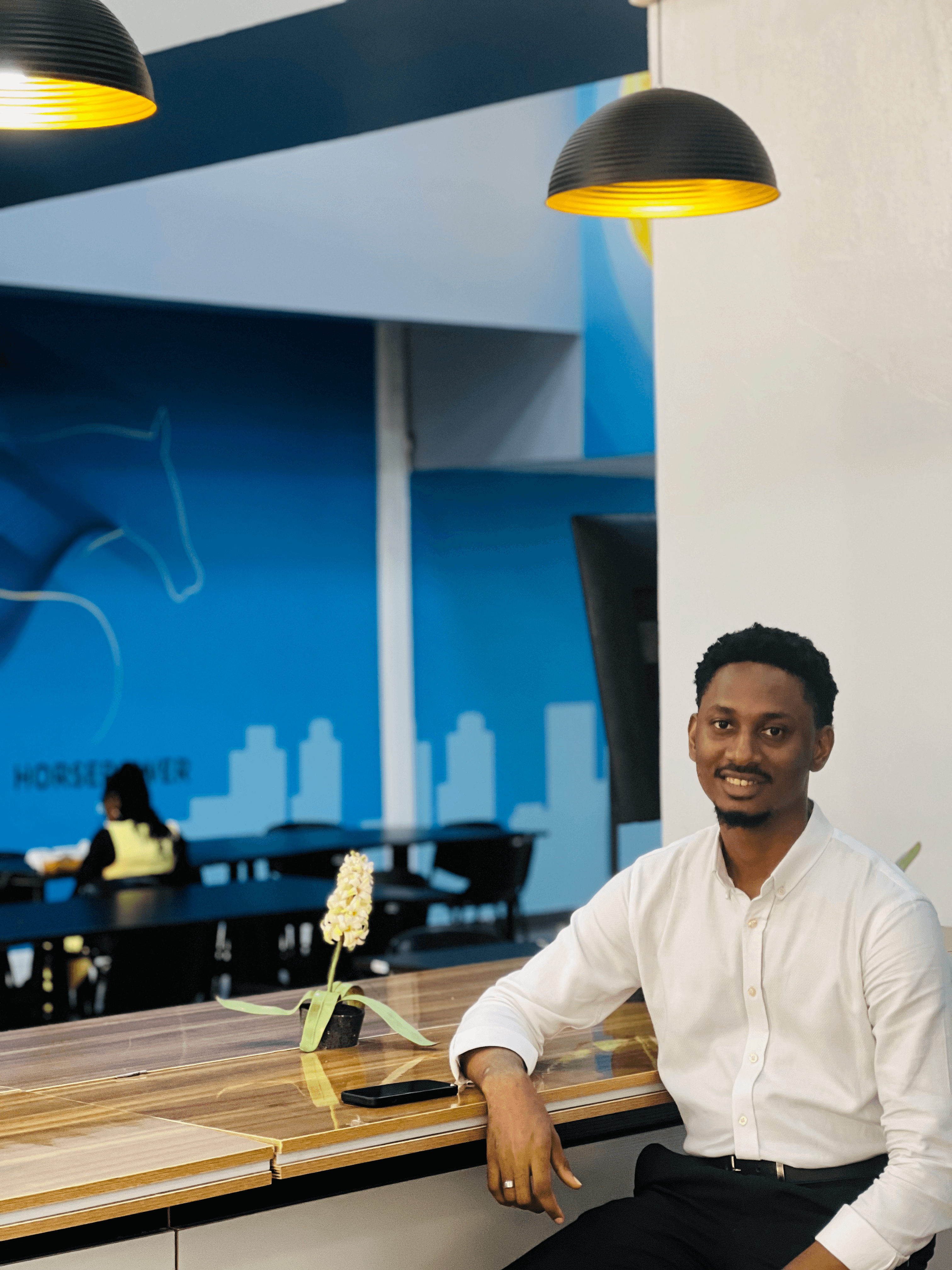 Smiling in a white button-down shirt at a vibrant blue co-working space.