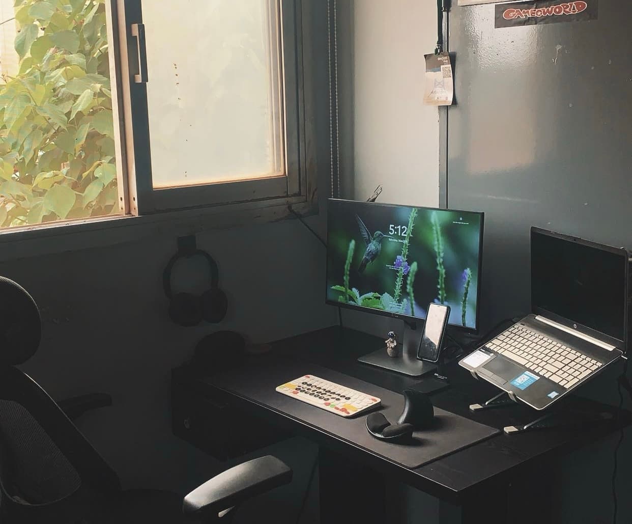 A cozy, aesthetic home office workspace setup featuring a monitor, laptop, split keyboard, and window view.